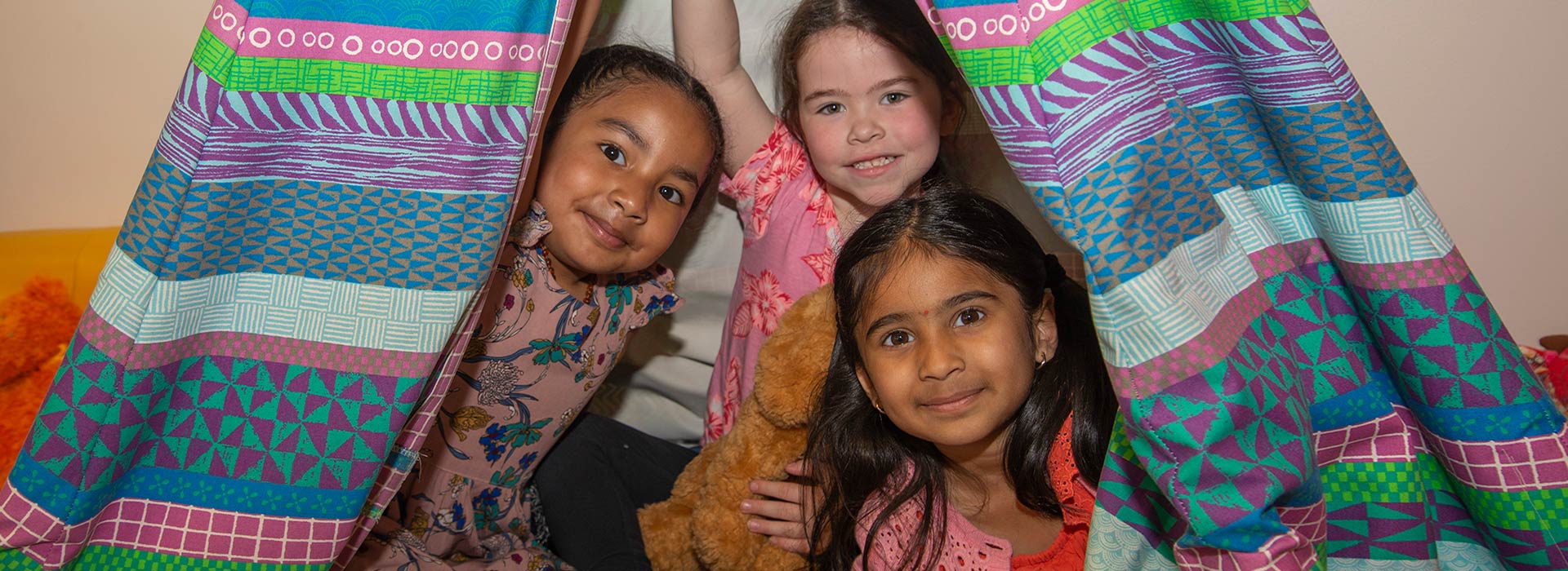 Three smiling girls playing together in a colourful teepee